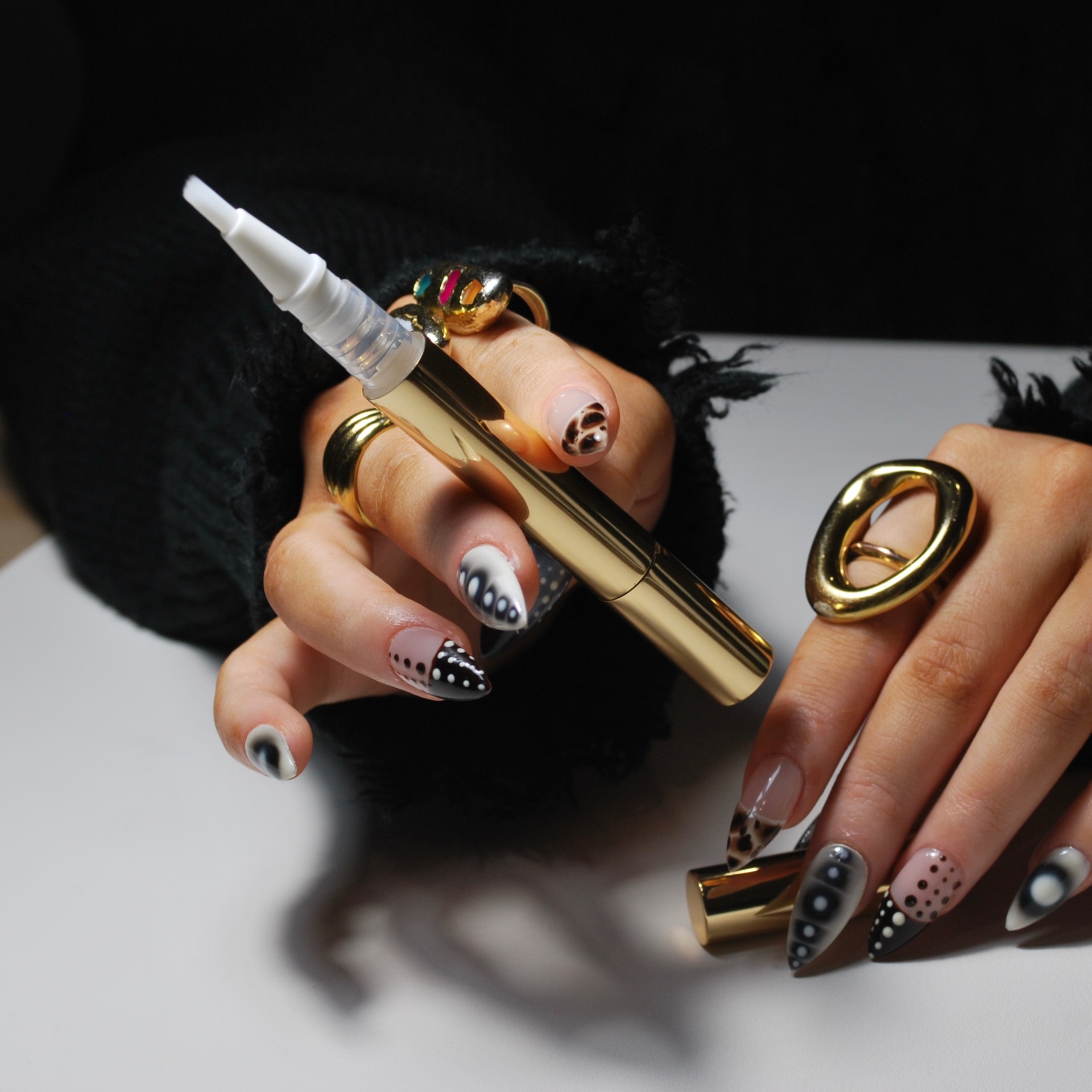 Gold and chrome cuticle serum pens on dark silk with eucalyptus