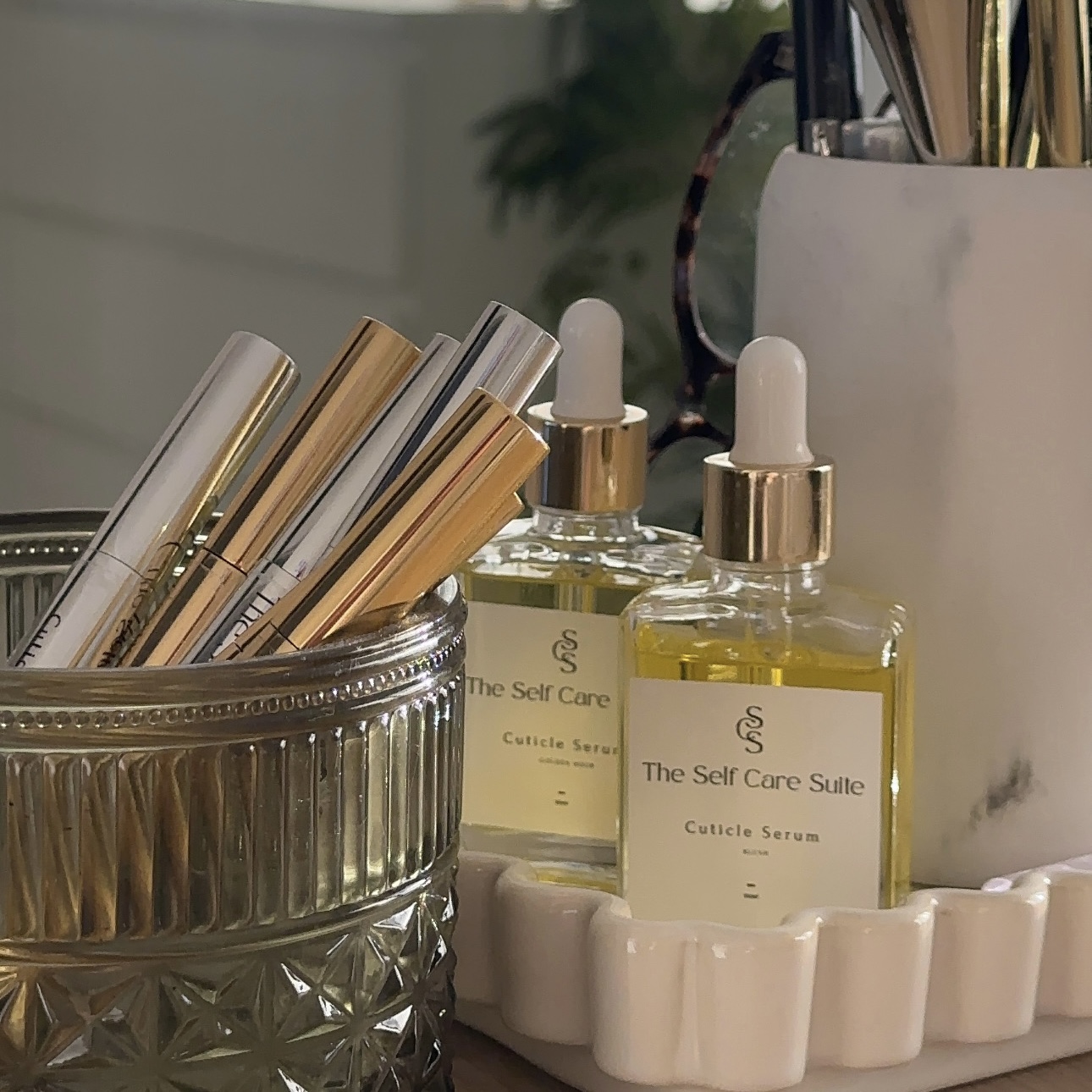 Cuticle serum bottles and gold and chrome pens styled on a marble vanity